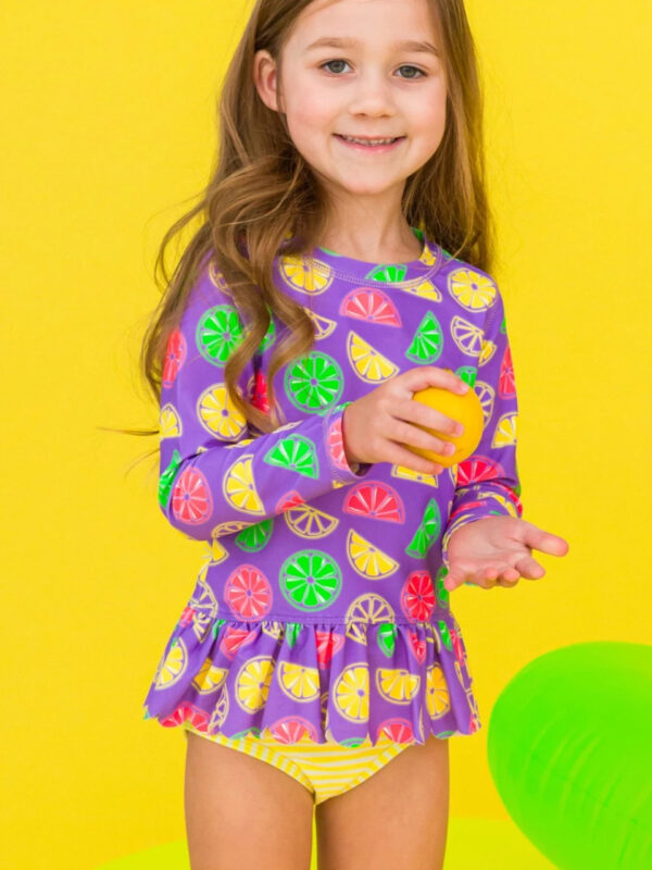 Girl in colorful citrus-patterned outfit, holding fruit.