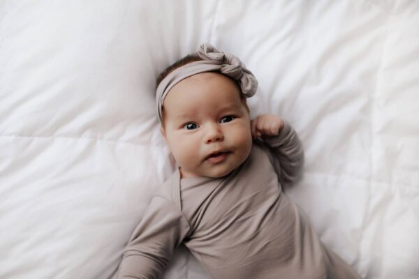 three little tots harbor mist taupe knotted gown Baby lying on white blanket in gray outfit.