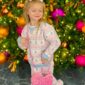 Child posing by festive Christmas tree with purse.