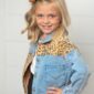 Child smiling in denim jacket with leopard print.
