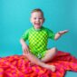 Smiling child on colorful blanket, turquoise background.