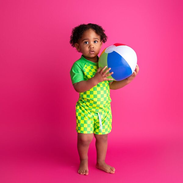 gigi and max brad green neon swim set Child holding a beach ball, bright pink background.