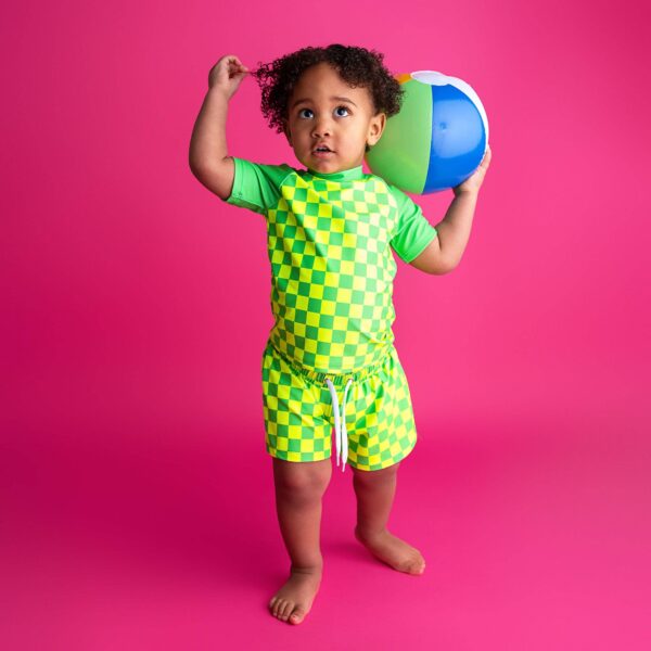 gigi and max brad green neon swim set Child in green checkered outfit holding beach ball.