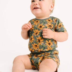Baby wearing sunflower-patterned outfit, smiling happily.