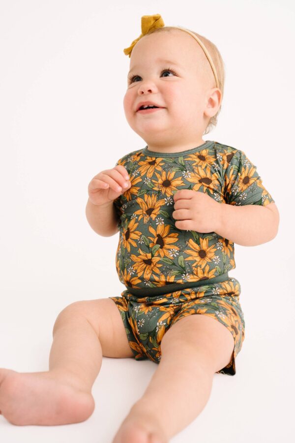 little one shop sunflower meadow bamboo shorts set Baby wearing sunflower-patterned outfit, smiling happily.