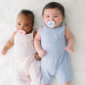 Two babies with pacifiers lying on soft material.