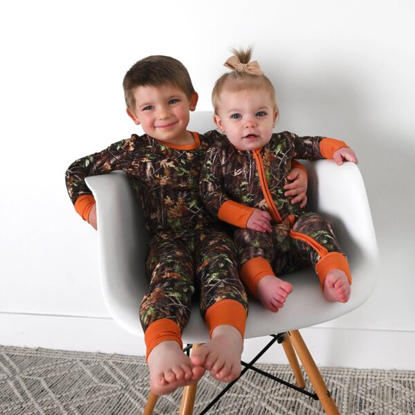 gigi and max hunter camo zip sleepies little bamboo baby outfit Children in camo pajamas sitting on chair.