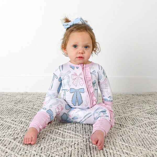 gigi and max samantha bows ruffle zip bamboo sleeplies little outfit Baby in bow-patterned pajamas sitting on carpet.