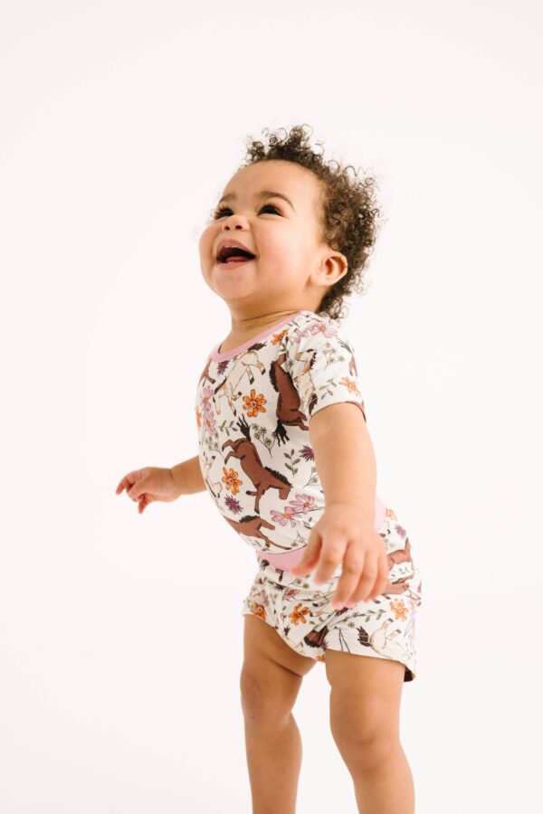 little one shop prairie ponies bamboo shorts set Smiling toddler in patterned bodysuit standing.