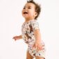 Smiling toddler in patterned bodysuit standing.