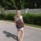 Woman wearing backpack walks on sunny sidewalk.