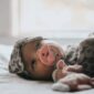 Baby with pacifier and stuffed toy on bed.