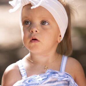 Young child wearing headband and necklace outdoors.