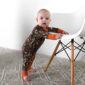 Baby in camouflage romper standing by chair.