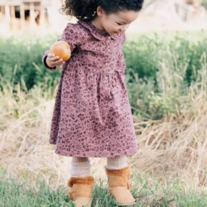 Child holding an apple outdoors, wearing patterned dress.