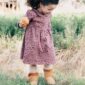 Child holding an apple outdoors, wearing patterned dress.