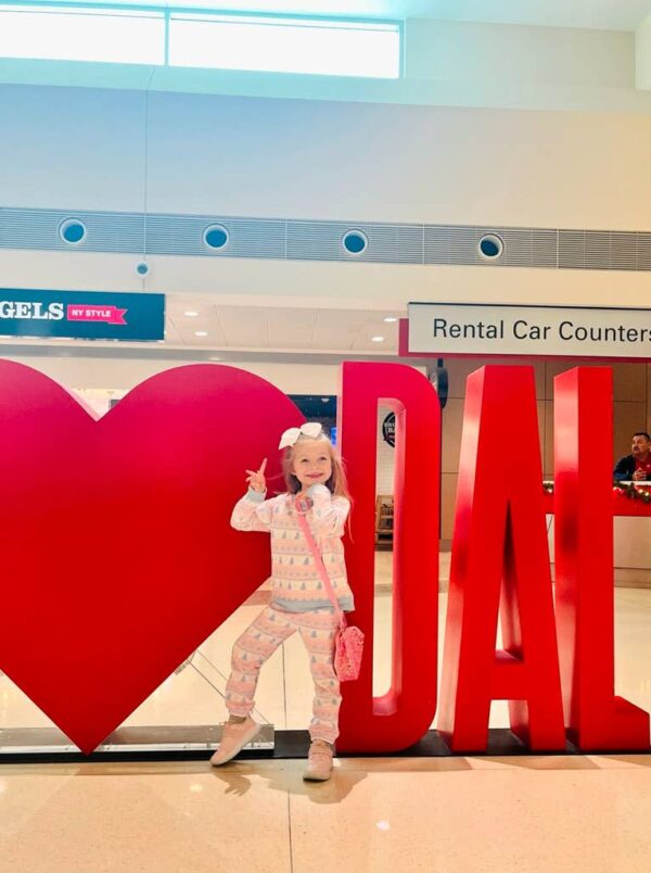 bits & bows sparkle heart purse Child posing by DAL airport sign.