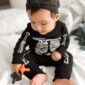Baby in skeleton outfit with pacifier on bed