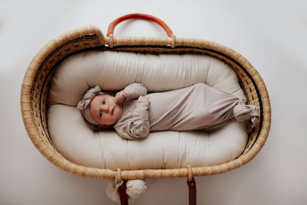three little tots harbor mist taupe knotted gown Baby in a wicker bassinet, wrapped and peaceful.