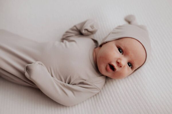 three little tots harbor mist taupe knotted gown Newborn baby in beige outfit lying down.