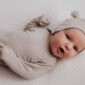 Newborn baby in beige outfit lying down.
