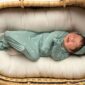 Newborn sleeping in basket, wearing green outfit.