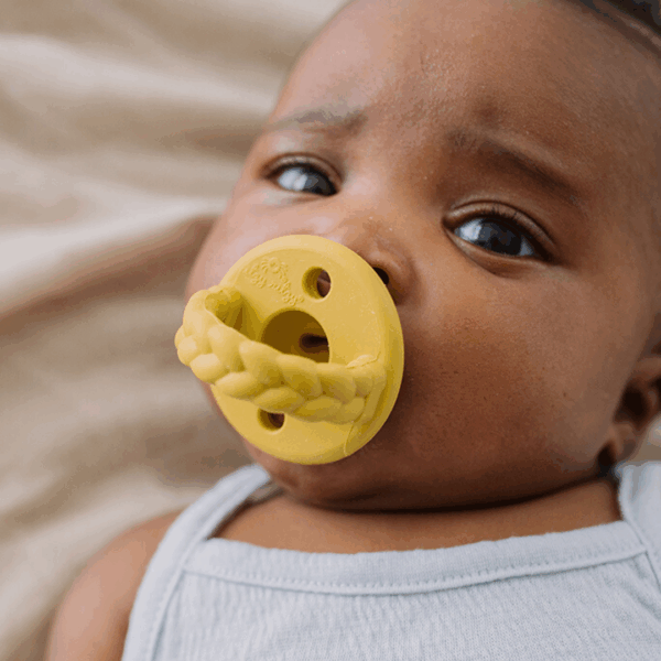 itzy ritzy sweetie soother™ pacifier sets (2 pack): agave + succulent cables Baby with yellow pacifier, wearing gray outfit.