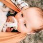 Baby in sling with pacifier outdoors.