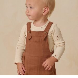 Toddler wearing brown overalls looking sideways