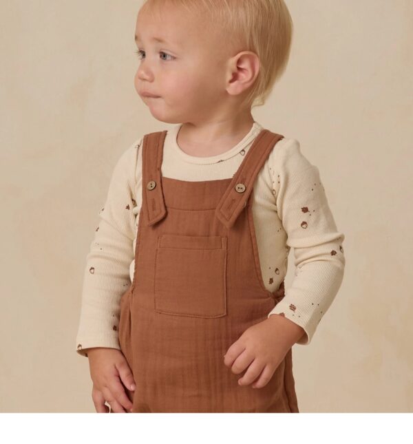 Toddler wearing brown overalls looking sideways