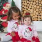 Two children in Santa outfits by fireplace.