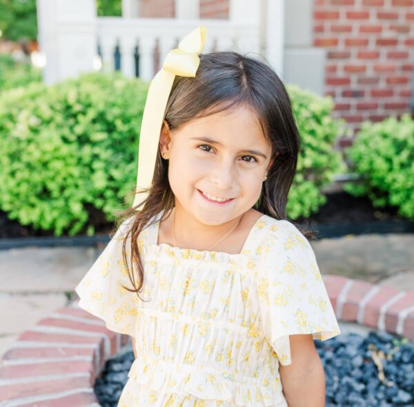 cherished moments kids 14k gold puff heart earrings Smiling child with yellow ribbon outdoors.