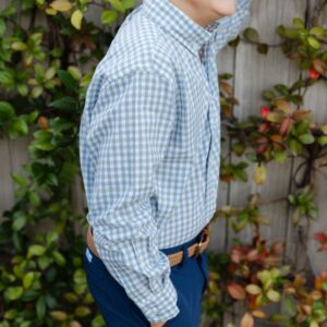 Smiling child in checkered shirt by leafy fence.