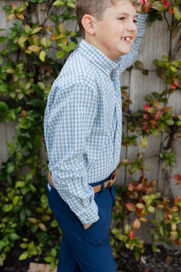 Smiling child in checkered shirt by leafy fence.