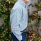 Smiling child in checkered shirt by leafy fence.
