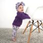 Baby in purple sweater standing by chair