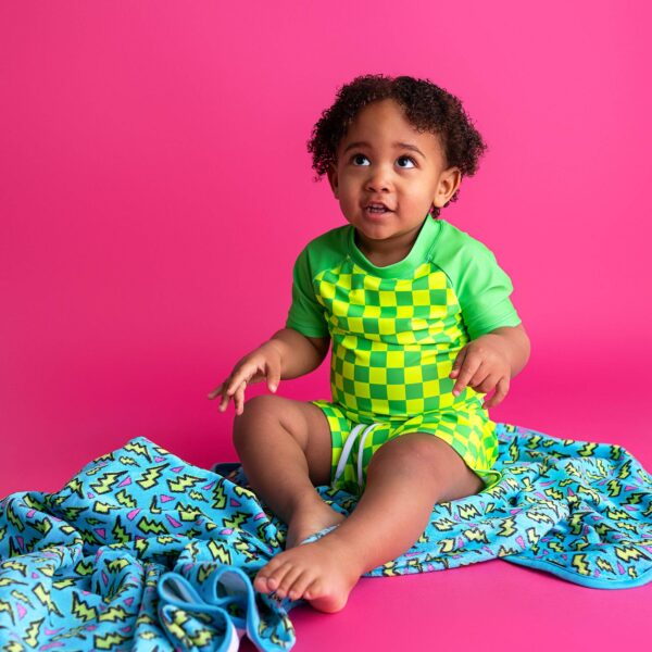 gigi and max brad green neon swim set Toddler in green checkered outfit on pink background.