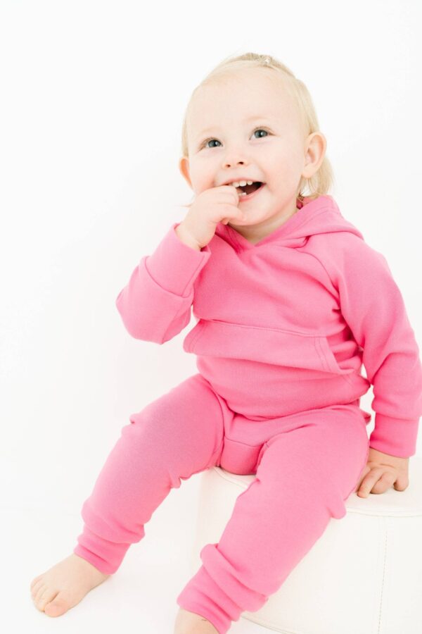 Smiling toddler in pink outfit sitting happily.
