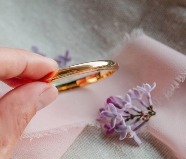 cherished moments gold classic bangle for baby & kids Hand holding golden ring with purple flowers.