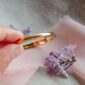 Hand holding golden ring with purple flowers.