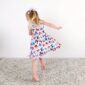 Child in floral dress twirls joyfully on carpet.