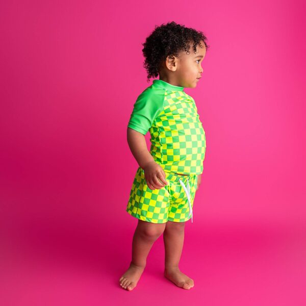 gigi and max brad green neon swim set Child in green-yellow checkered swimsuit on pink background.