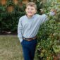 Smiling child standing by garden hedge.