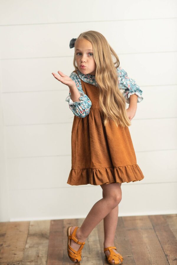 wren & james kids blue floral smocked top & caramel corduroy jumper set Child blowing a kiss, wearing brown dress.