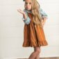 Child blowing a kiss, wearing brown dress.