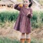 Child holding apple, standing in grassy field.