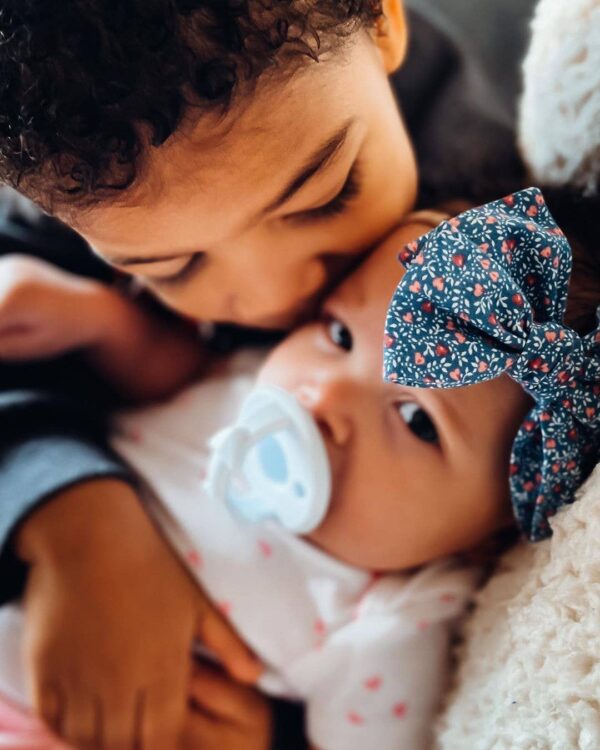 itzy ritzy sweetie soother™ pacifier sets (2 pack): agave + succulent cables Child cuddling baby with pacifier and bow.