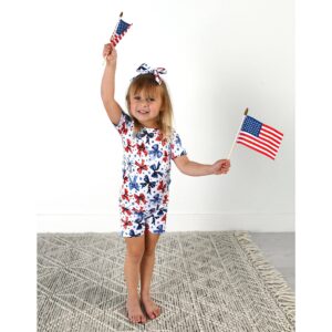 Child waving American flags joyfully in printed outfit.