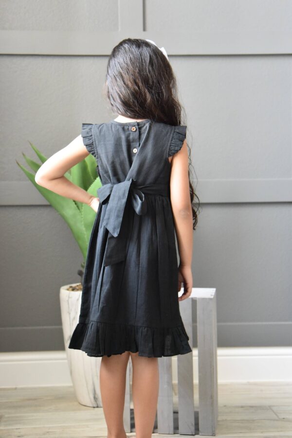 Child in black dress with bow, back view.
