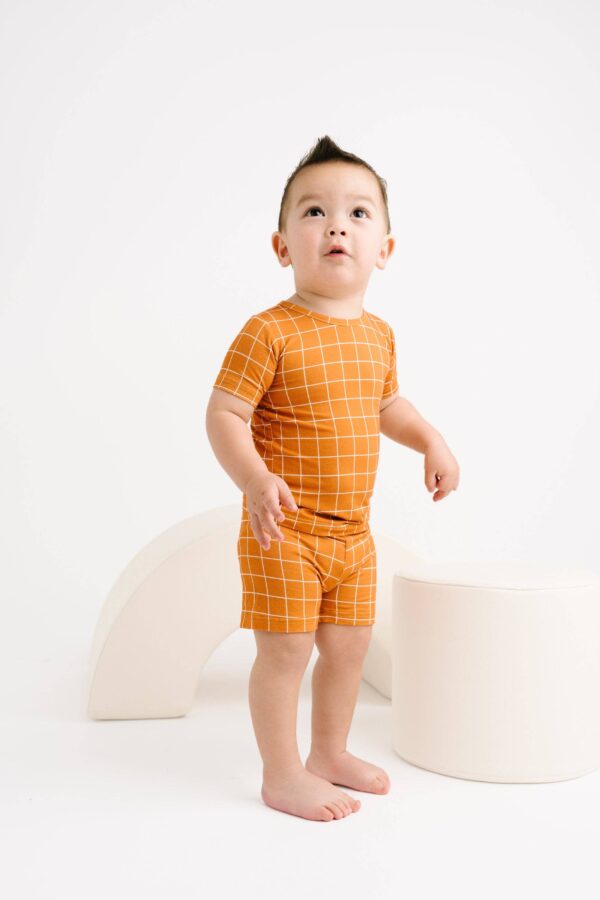 little one shop rust checks bamboo shorts set Child in orange plaid outfit standing indoors.